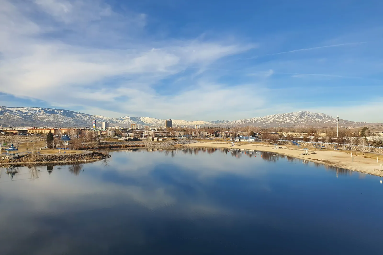 Downtown Reno and the snow-capped Sierra reflected in a calm lake under a wide blue sky