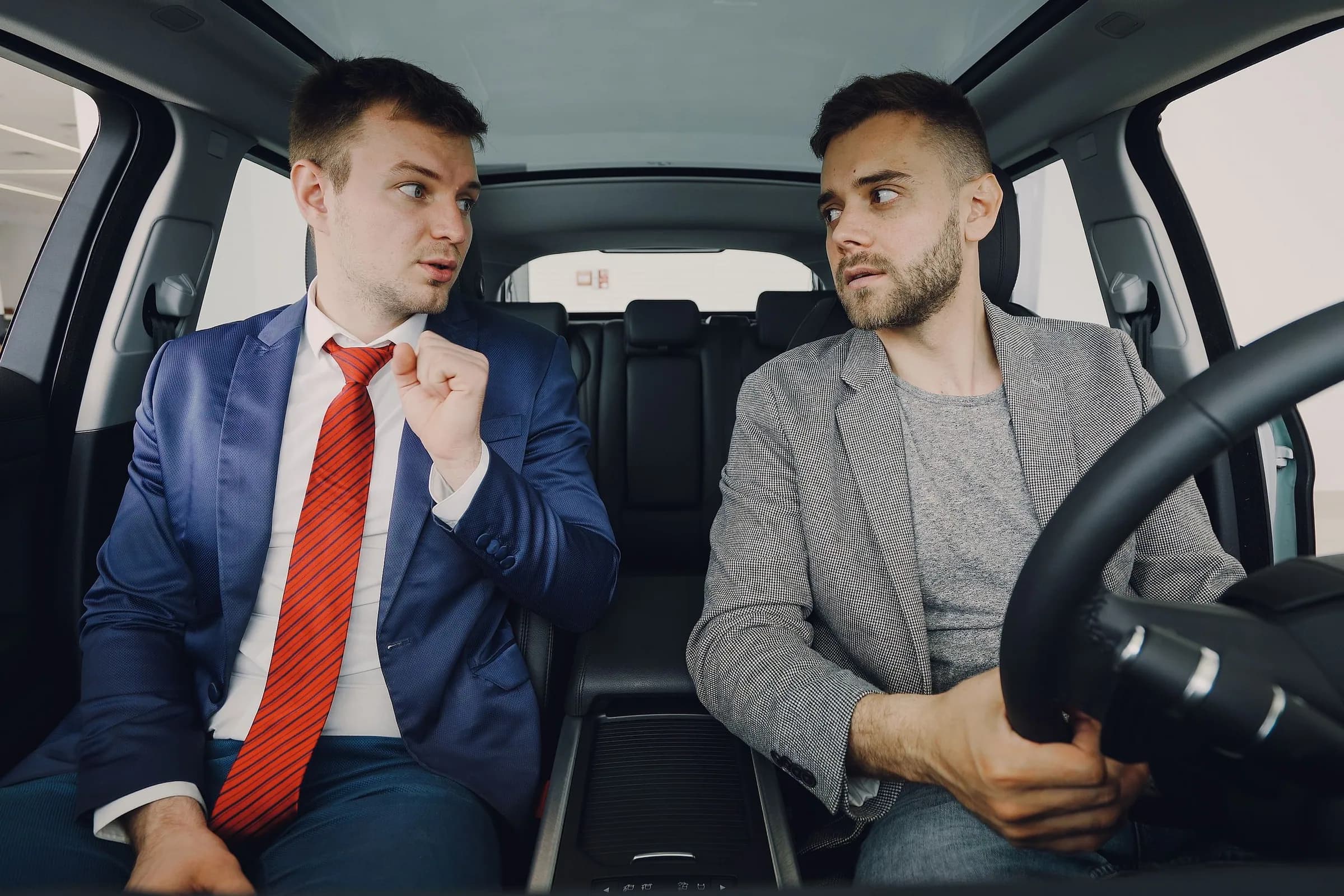 Two colleagues in jackets talking in the front seats of a car, one at the wheel