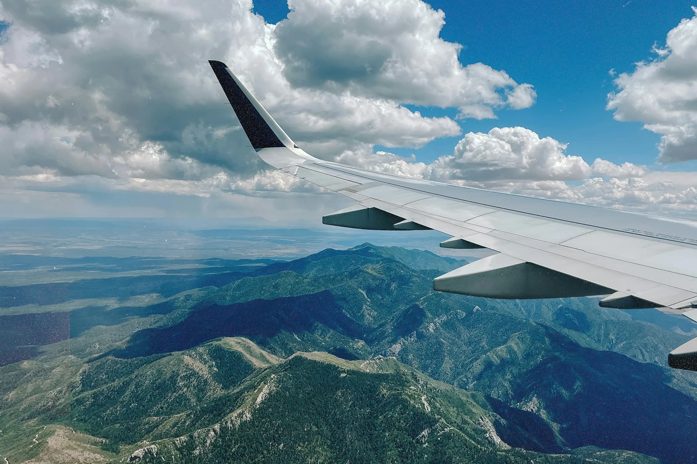 An airliner’s wing over forested mountain ridges, with a wide high-desert valley beyond
