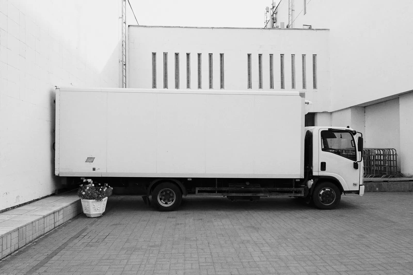 White box truck parked beside a white building